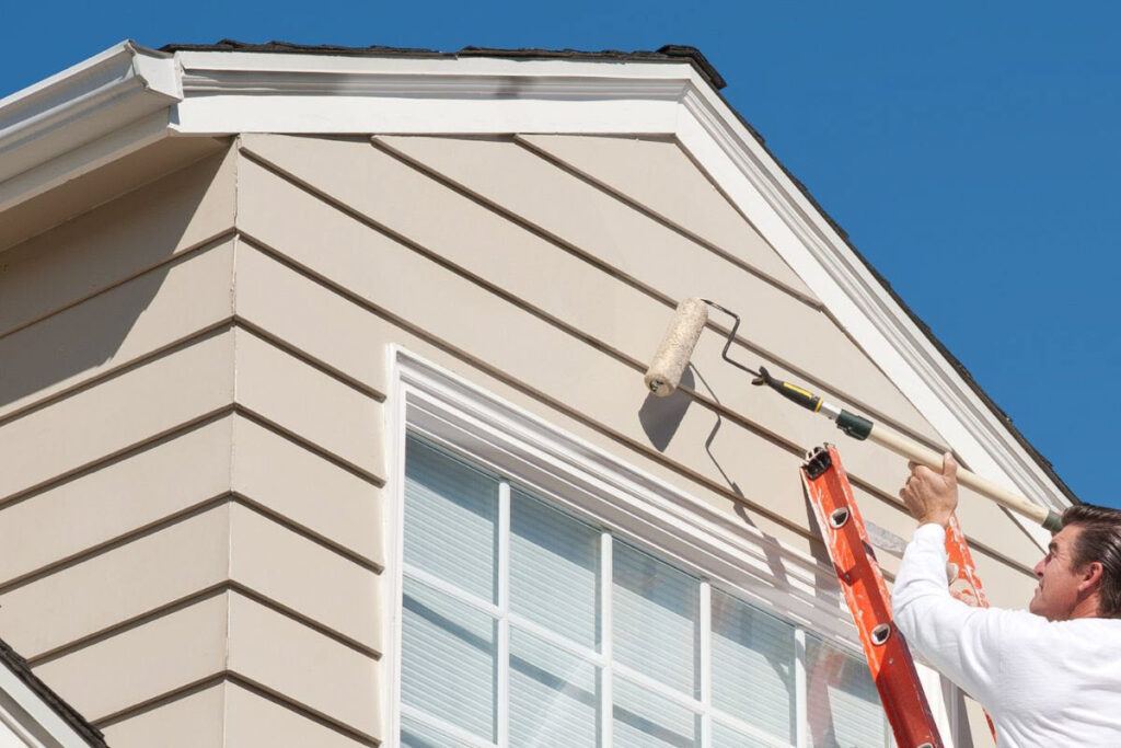 Professional Painter Painting The Exterior Of A Property In Beige